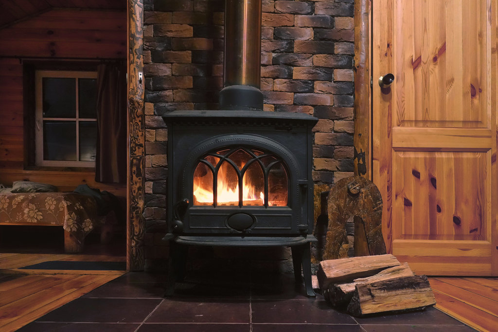 un poele à bois chauffe au centre de la photo dans une maison de style rustique avec principalement une décoration boisée.