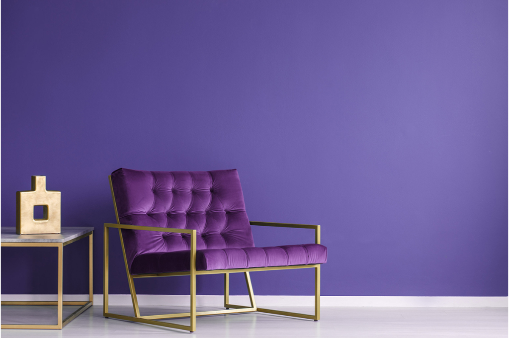 plan sur un fauteuil violet à barres métalliques dorés posé devant un mur violet.