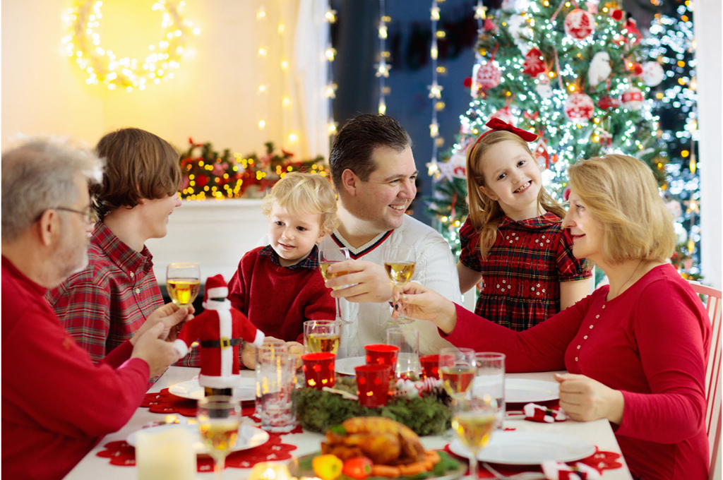 table du réveillon de Noël sur laquelle une famille est en train de manger. on y distingue les grands-parents qui trinquent, un adule homme et 3 enfants dont 2 en bas âge.