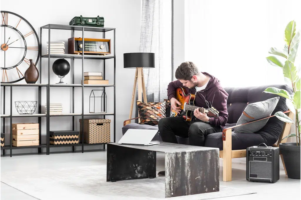 un musicien qui joue de la guitare est assis sur un canapé noir dans un salon de style industriel.