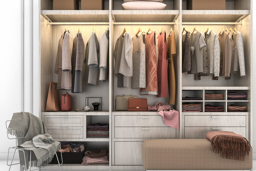 vue sur une grande armoire avec des vêtements sur cintres, des tiroirs et étagères bien rangées avec des vêtements et accessoires à leur place. une chaise est posée à côté avec un plaid gris.