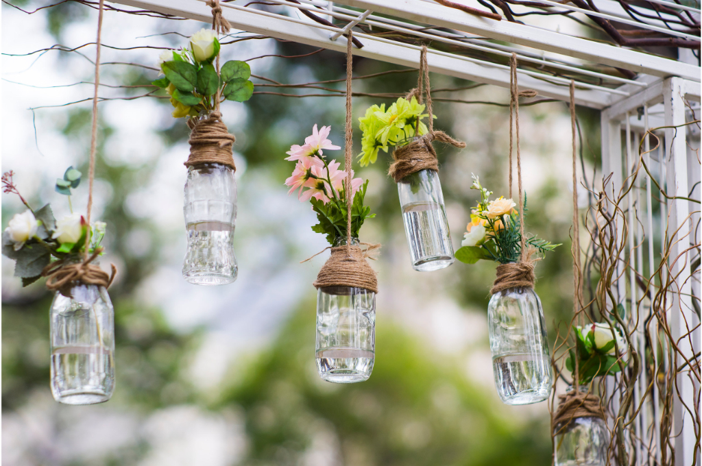 des bouteilles en verre contenant de l'eau et des fleurs, sont suspendues par une corde.