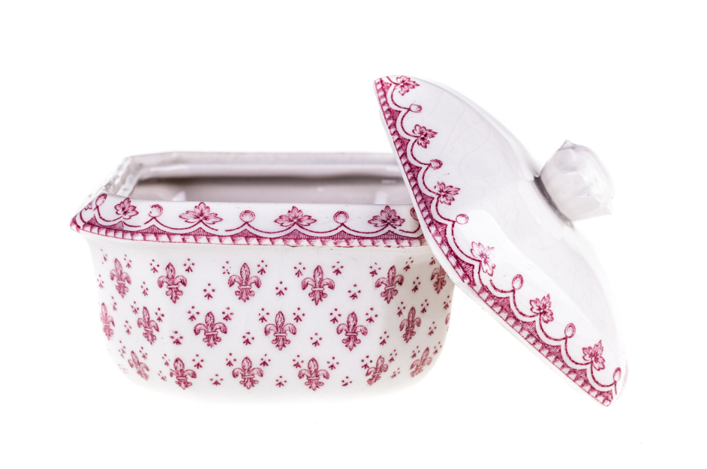 vue rapprochée sur une porcelaine blanche avec des motifs roses foncés. elle est ouverte avec le couvercle posé à moitié dessus.