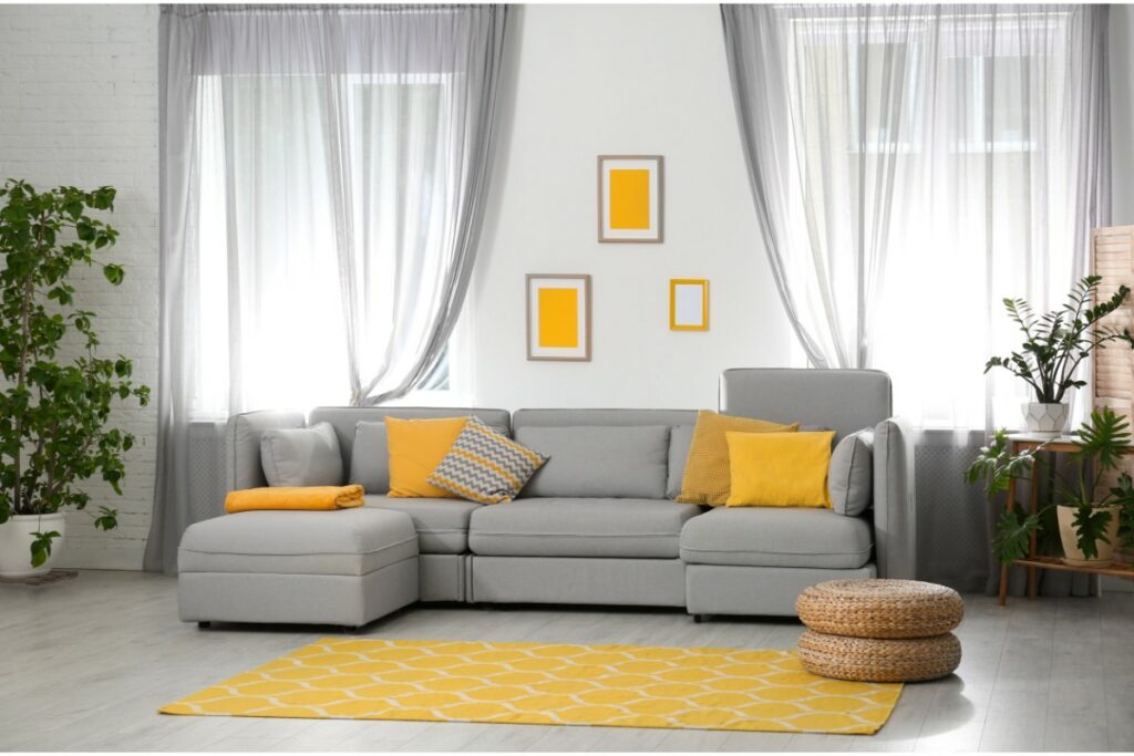 salon gris et jaune avec un canapé gris et des coussins jaunes. les rideaux sont gris. le tapis devant le canapé est jaune à formes géométriques.