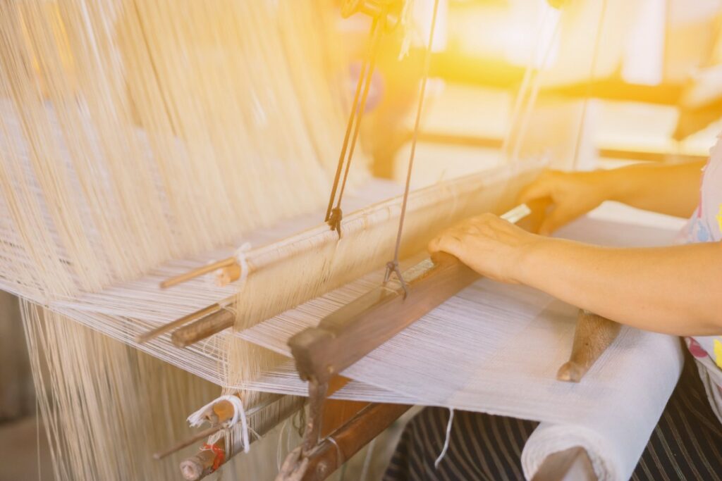 une personne, dont on ne voit que les bras, utilise une machine à tisser en bois à l'ancienne. 