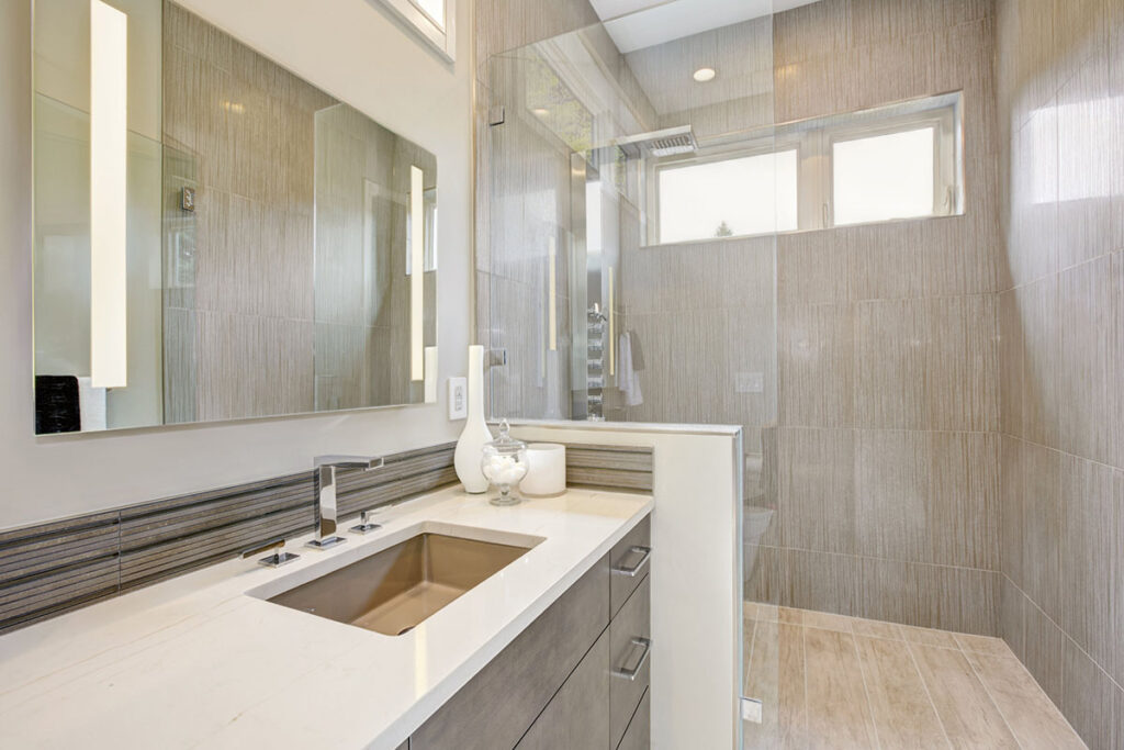 salle de bains avec un grand miroir au-dessus du lavabo/ on voit une douche à l'italienne au fond de la pièce.