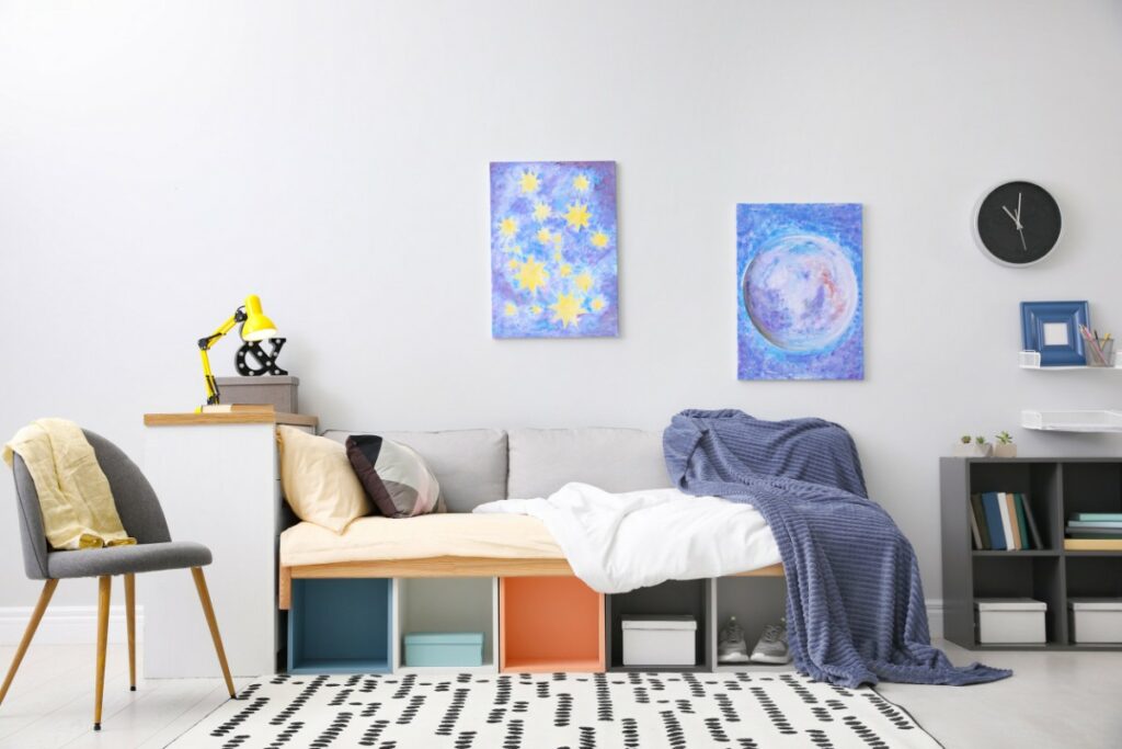 photo d'une pièce avec divers éléments de décoration. 2 peintures sont accrochés sur un mur ainsi qu'une horloge noire et une petite étagère. un canapé a été créé avec des coussins posés sur des cubes de rangement.