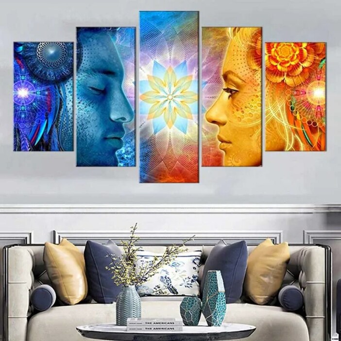 Tableau visage femme et homme face à face coloré accroché dans un salon à la décoration classique avec un canapé aux nombreux coussins colorés bleu, jaune et avec une table basse et des vases de couleur