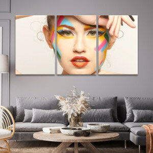 Tableau visage contemporain avec maquillage multicolore accroché au mur gris d'un salon classique au-dessus d'un canapé d'angle gris et d'une table basse en bois décorée avec un vase