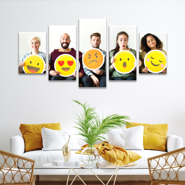 Tableau visage associé à son expression en émoticône affiché au mur blanc d'un salon avec canapé et coussins jaunes, table basse décorée d'une plante verte et fauteuils en rotin