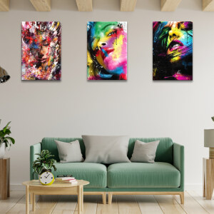 Tableau visage graffiti de femme multicolore accroché dans un salon avec poutres au plafond et canapé vert tendre en bois clair assorti à une table basse
