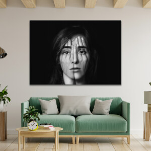 Tableau visage surréaliste accroché dans un salon avec poutres et mobilier en bois clair dont un canapé aux coussins vert tendre et une table basse
