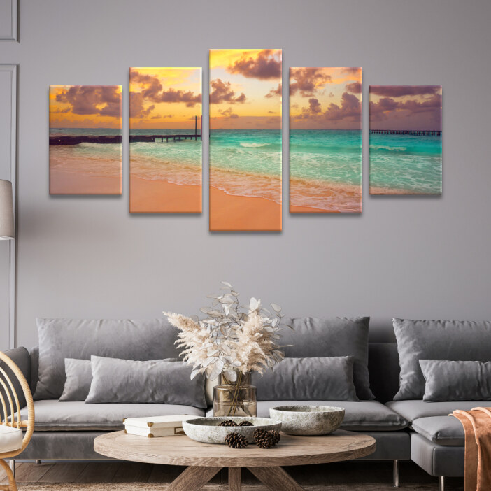 Tableau Mexique magnifique coucher de soleil à Cancún accroché dans un salon de style classique sur un mur gris au-dessus d'un canapé gris d'angle encadrant une table basse ronde en bois clair avec un bouquet de fleurs séchées.