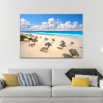 Tableau Mexique plage de Delfines à Cancún affiché au-dessus d'un canapé crème agrémenté de coussins jaunes et à rayures.