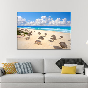 Tableau Mexique plage de Delfines à Cancún affiché au-dessus d'un canapé crème agrémenté de coussins jaunes et à rayures.