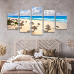 Tableau Mexique plage tropicale à Cancún affiché dans une chambre sur un mur beige au-dessus d'un lit avec tête de lit en rotin et draps beiges.