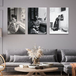 Tableau Mexique portrait de Frida Kahlo à la fenêtre en noir et blanc accroché dans un salon de style classique aux murs et au canapé d'angle gris avec une table basse en bois décorée d'un bouquet de fleurs séchées.