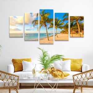 Tableau Mexique plage de palmiers aux Caraïbes accroché au mur blanc d'un salon avec canapé blanc à coussins jaunes et table basse en verre avec plante verte posée dessus.