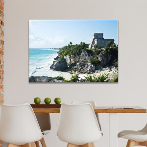 Tableau Mexique site Maya de Tulum affiché dans une cuisine sur un mur blanc derrière une table en bois avec des pommes vertes posées dessus et entourée de chaises blanches.