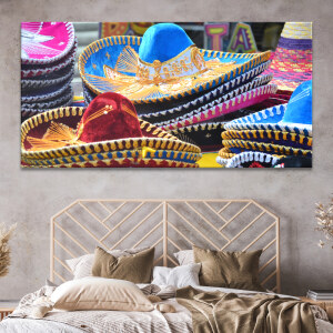 Tableau Mexique sombreros colorés empilés au marché accroché au mur beige d'une chambre au-dessus d'une tête de lit en rotin moderne.
