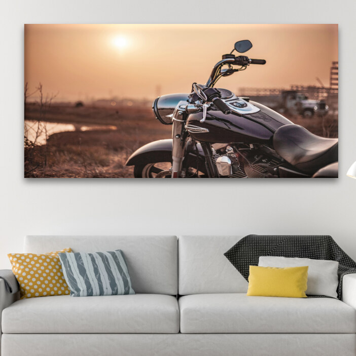 Un tableau d'une moto Harley Davidson au coucher du soleil accroché au-dessus d'un canapé de salon.